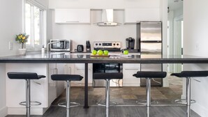 A modern kitchen with a central island, bar stools, stainless steel appliances, and a large window. - Outpost: Sleeping Indian W5 (Teton Village)