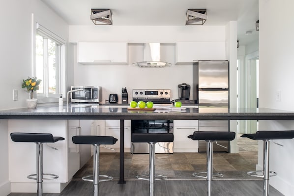A modern kitchen with a central island, bar stools, stainless steel appliances, and a large window. - Outpost: Sleeping Indian W5 (Teton Village)