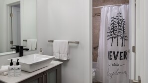 A bathroom with a white sink, two bottles of lotion, a towel, and a shower curtain with a tree design. - Outpost: Sleeping Indian W5 (Teton Village)