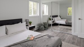 A modern bedroom with a large bed, a nightstand, a mirror, and a window. - Outpost: Sleeping Indian W5 (Teton Village)