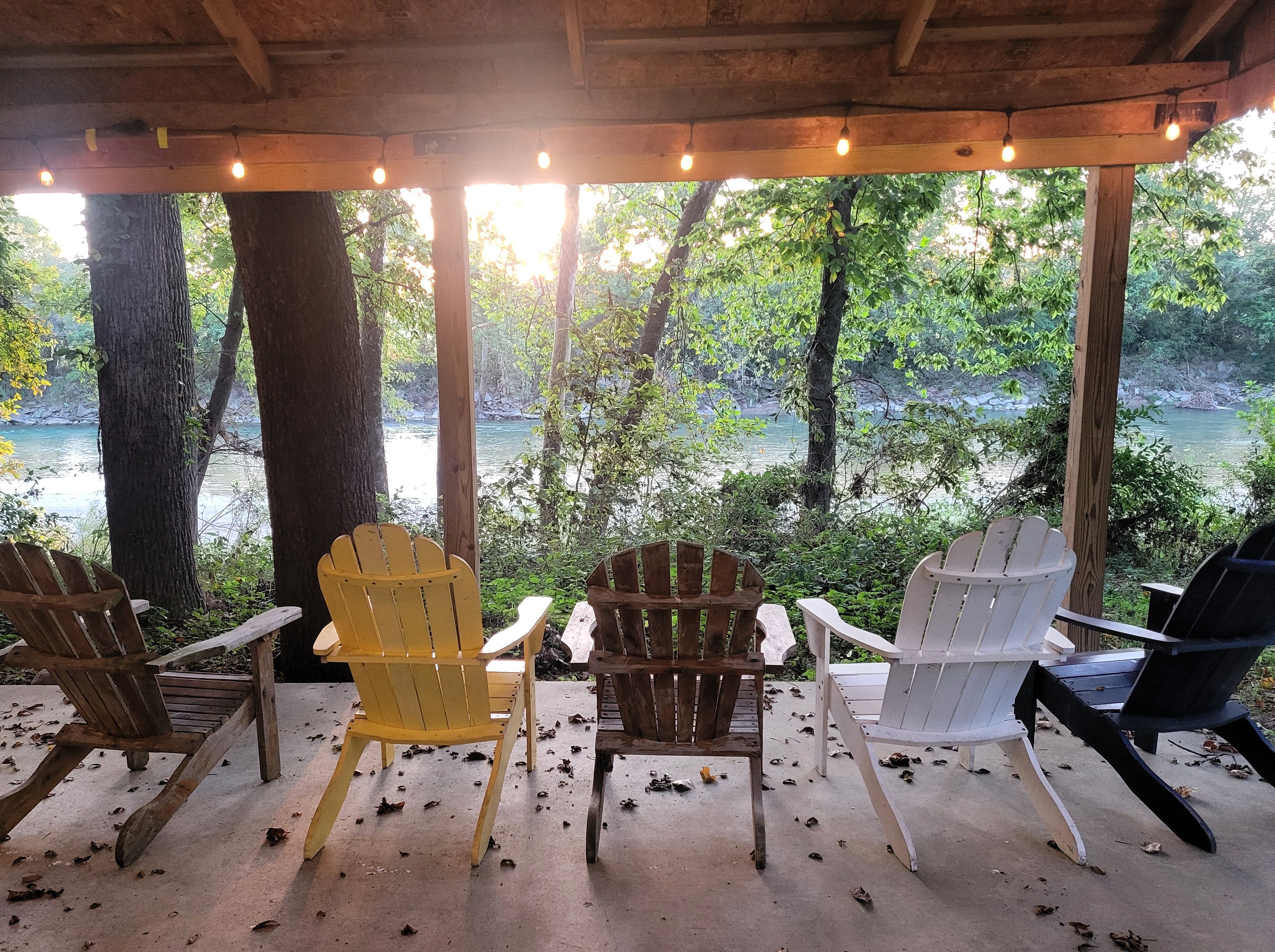 Un espace de repos abrité, avec des chaises disposées face à une rivière, le tout entouré d’arbres.