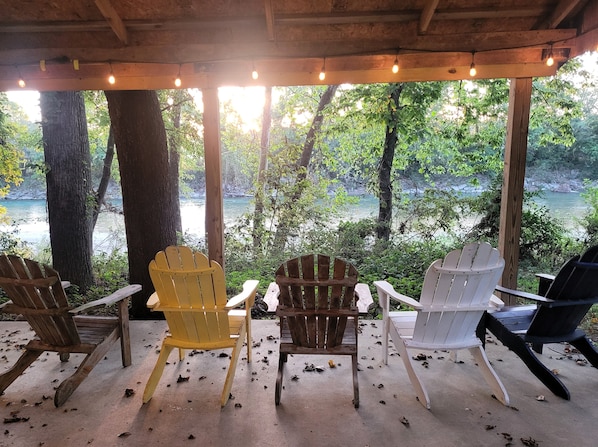 A covered seating area with chairs facing a river, surrounded by trees.