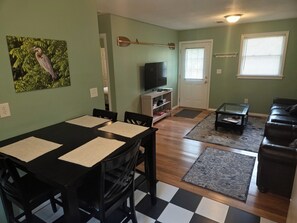 A living room with a dining table, black chairs, a television, a coffee table, and a couch.