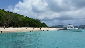 Um barco chamado 'Betty Anna' em águas azul-turquesa próximo a uma praia de areia, com pessoas nadando e caminhando.