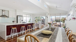Een ruime keuken met een centraal kookeiland, barstoelen en een eethoek met een lange tafel en stoelen.