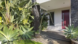 Een modern huis met een gevel van natuursteen, een rode deur en weelderige tropische planten in de tuin.