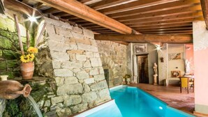 Une piscine intérieure aux murs en pierre, dotée d’un plafond en bois et d’un décor rustique.
