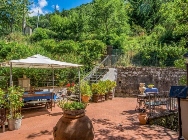 An outdoor patio with a covered seating area, potted plants, and a stone wall.