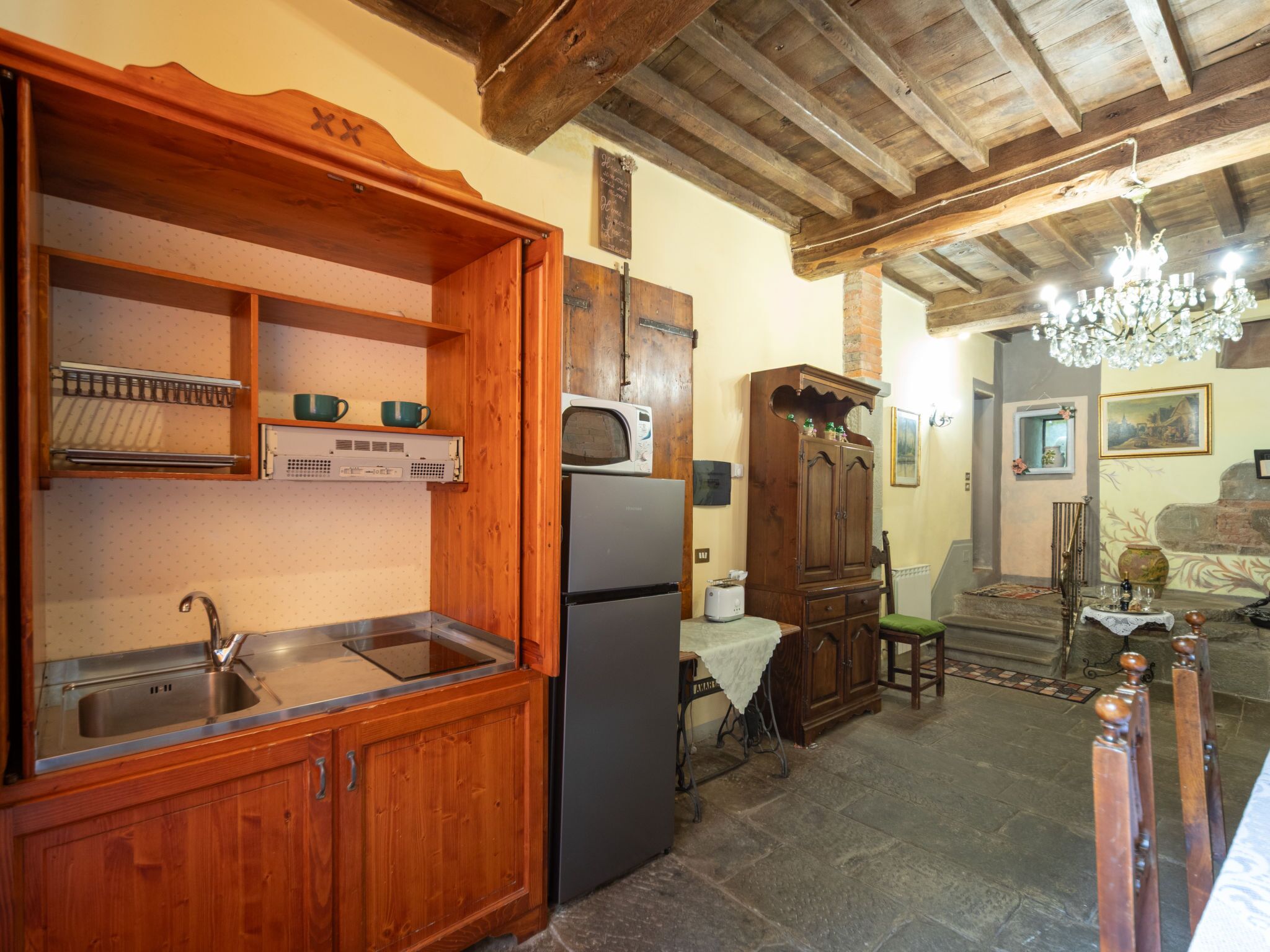 A rustic kitchen with wooden cabinets, a refrigerator, and a chandelier.