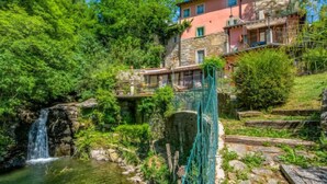 Un bâtiment rustique en pierre, doté d’une façade rose, d’une cascade et d’une végétation luxuriante.