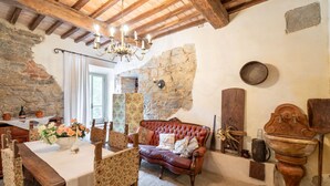 Un intérieur rustique avec des murs en pierre apparentes, un plafond en bois, un canapé en cuir et une table à manger avec des chaises.