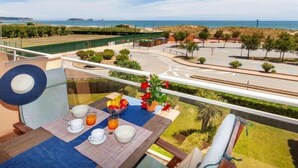 Un balcon avec une table préparée pour le petit-déjeuner, donnant sur une route côtière et une plage.
