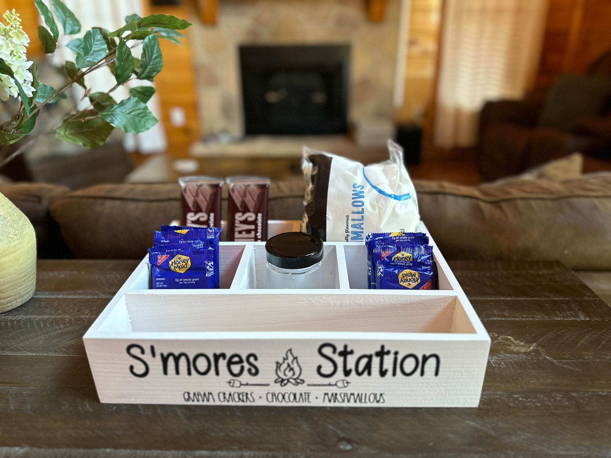 A wooden box labeled 'S'mores Station' with items like chocolate bars, marshmallows, and graham crackers.