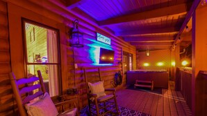 A log cabin interior with a wooden exterior, a large window, a mounted TV, and a hot tub area. - 5min Dollywood~Easy Road~FirePit~Arcade~Playground (Sevierville)