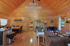 A wooden cabin interior with a dining area, kitchen, and living space.