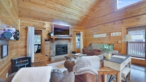 A cozy log cabin interior with a fireplace, wooden walls, a television, and comfortable seating. - 5min Dollywood~Easy Road~FirePit~Arcade~Playground (Sevierville)