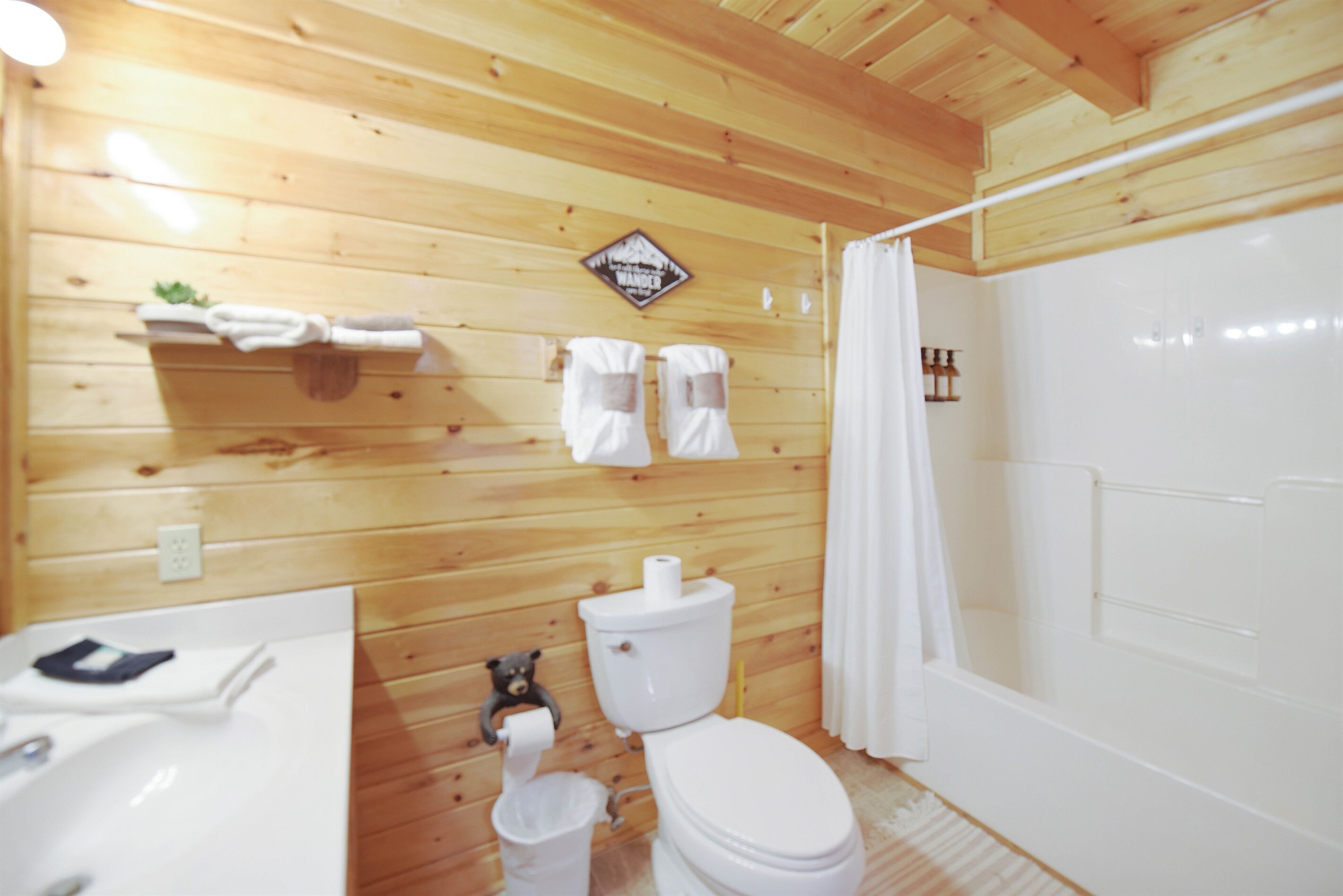 A wooden-paneled bathroom with a toilet, sink, and shower curtain.