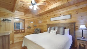 A wooden cabin bedroom with a bed, a nightstand, a ceiling fan, and a window with curtains. - 5min Dollywood~Easy Road~FirePit~Arcade~Playground (Sevierville)