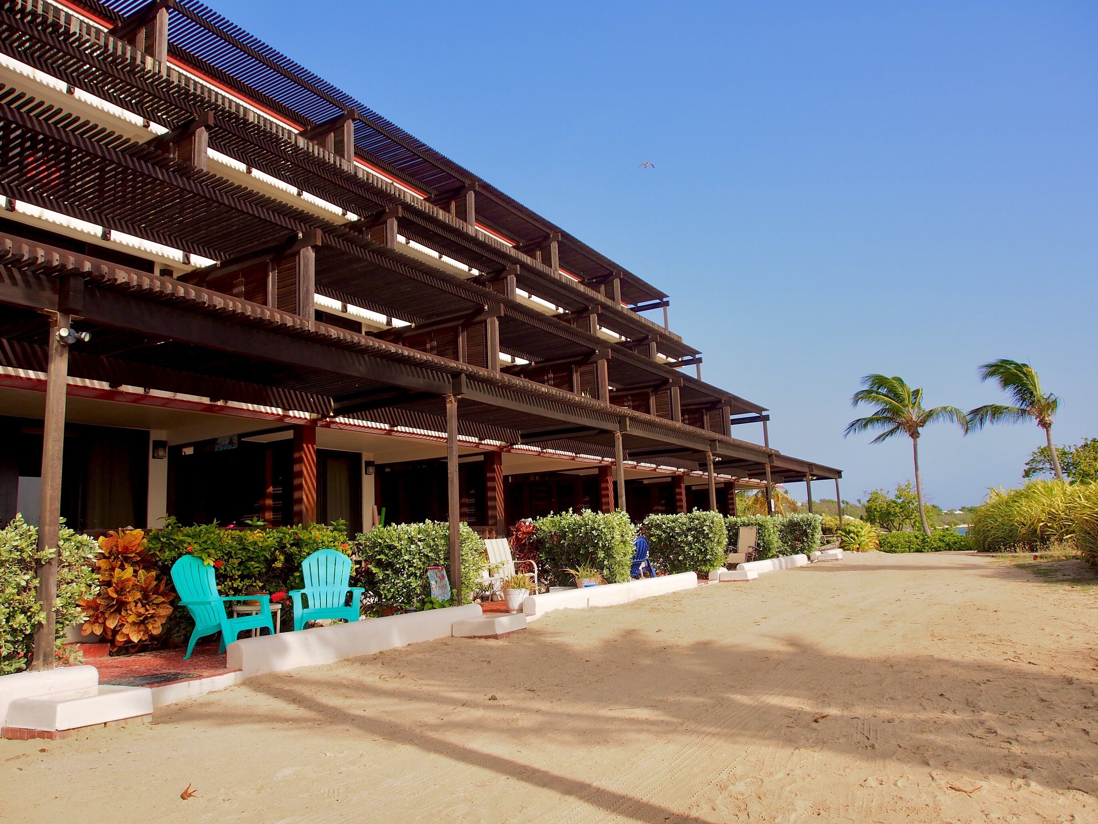 A multi-story building with a covered outdoor area, featuring a sandy ground and potted plants.