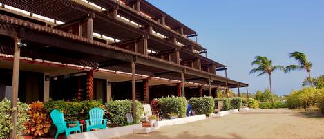 A multi-story building with a covered outdoor area, featuring a sandy ground and potted plants.