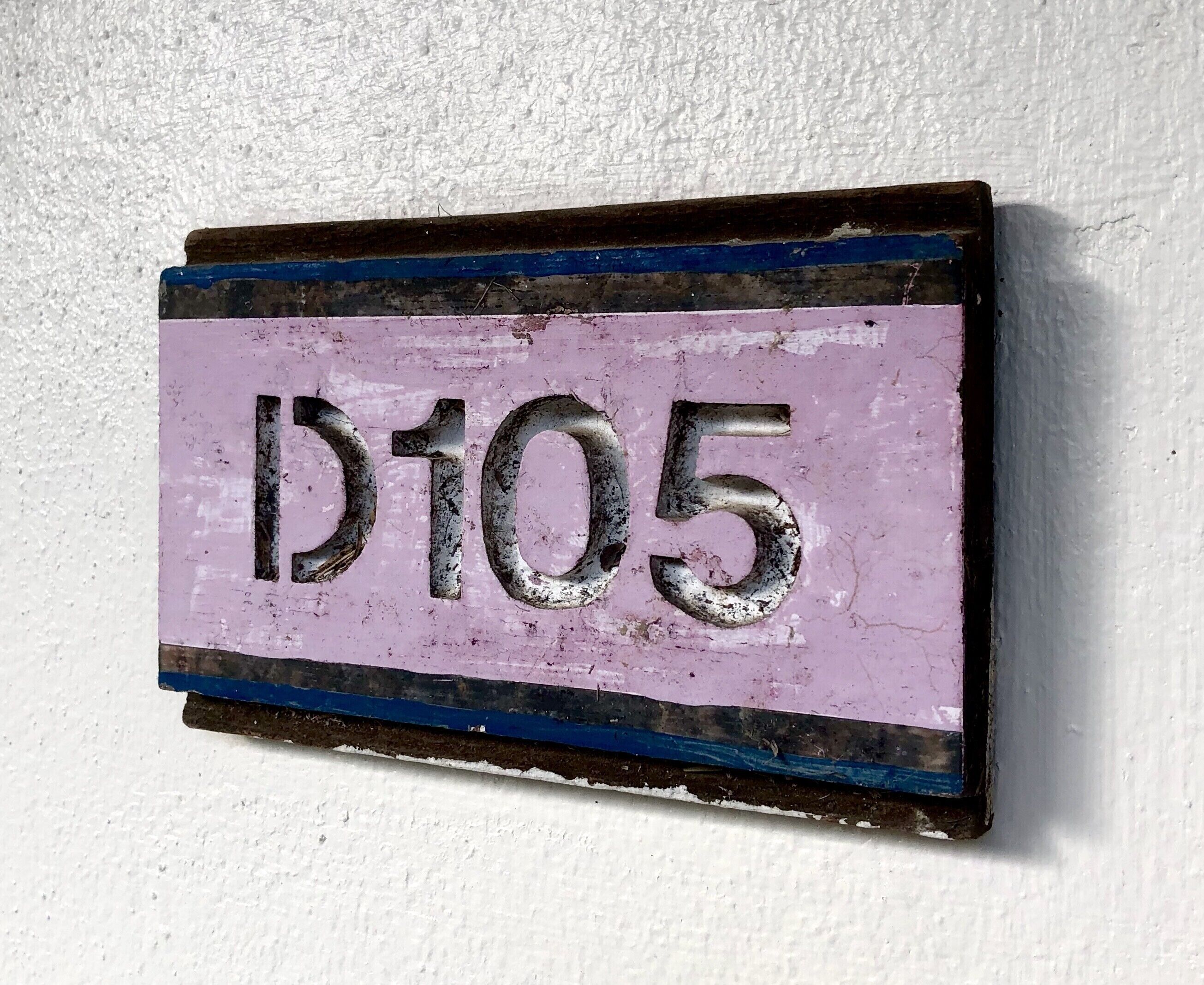 A wall-mounted sign with the number "D105" on a pink background with blue and black borders.