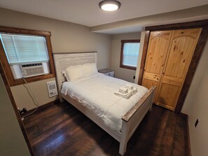 Ein Schlafzimmer mit einem Bett, einem Holzschrank und einem Fenster mit Jalousien.