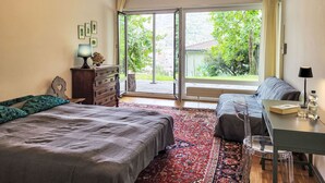 Une chambre avec un grand lit, un bureau et une vue sur la verdure.