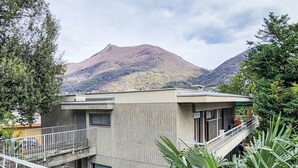 Un bâtiment moderne doté d’un balcon, entouré de verdure et avec des montagnes en arrière-plan.