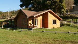 A wooden cabin with a sloped roof, a porch, and a fenced yard. - beach shore hut (lago ranco)