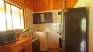 A compact kitchen with wooden cabinets, a built-in microwave, and a refrigerator. - beach shore hut (lago ranco)