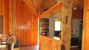 A wooden interior with a bar area, wooden flooring, and a kitchen visible through an open doorway. - beach shore hut (lago ranco)