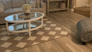 Ein Wohnzimmer mit einem beigen Sofa, einem Glastisch, einem gemusterten Teppich und einer Tür im Hintergrund.