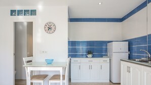 Une cuisine avec des meubles blancs, un plan de travail recouvert de carreaux bleus, un réfrigérateur blanc et une table à manger avec des chaises.