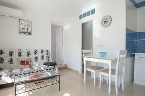 Un salon comprenant un canapé, une table basse en verre, une table à manger avec des chaises, et un coin cuisine avec un évier et des placards.