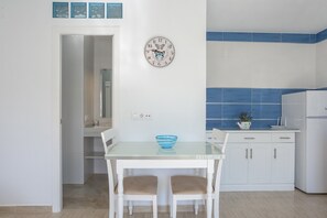 Une cuisine avec une table blanche, deux chaises, une horloge et un crédence bleue carrelée.