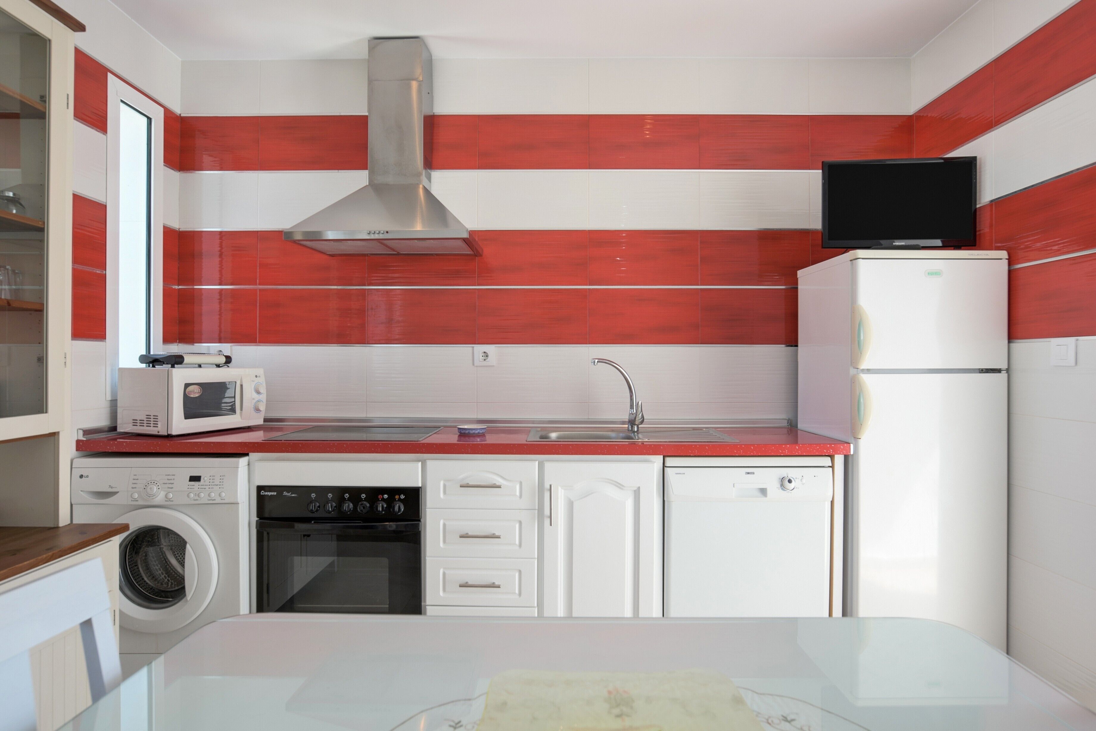 Eine kleine Küche mit Mikrowelle, Backofen, Geschirrspüler und einem Fernseher auf dem Kühlschrank.
