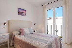 Un dormitorio con cama, mesitas de noche, un cuadro y un balcón con vistas.