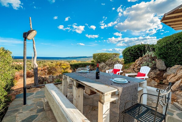 An outdoor dining area with a table and chairs, a bench, and a view of the landscape. - Apartment "Cala Brandinchi" with Sea View, Private Terrace and Shared Pool (San Teodoro)