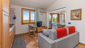 A compact living space with a kitchenette, a sofa with a red blanket, a television, and a dining area with a view.