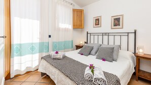 A bedroom with a bed, curtains, a wooden cabinet, two framed pictures, a bedside table, and a nightstand.
