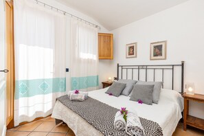 A bedroom with a bed, curtains, a wooden cabinet, two framed pictures, a bedside table, and a nightstand.