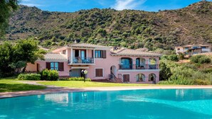 A large house with a swimming pool, surrounded by lush greenery and hills.