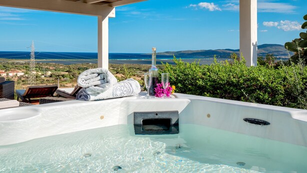 A hot tub with a view of the sea, a towel, and a bottle.