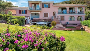 A two-story house with a balcony, a staircase, and a garden with pink flowers.