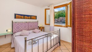 Ein Schlafzimmer mit Bett, Nachttisch, Fenster mit Blick auf Grünflächen und Kunstwerk an der Wand.