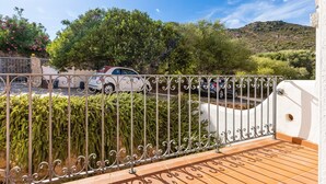 Ein Balkon mit Metallgeländer, Fliesenboden und Blick auf geparkte Autos und Grünflächen.