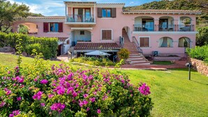 Ein zweistöckiges Haus mit Balkon, Treppe und einem Garten mit rosa Blumen.