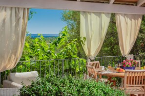 Uma área de estar coberta ao ar livre, com mesa, cadeiras e vista para a paisagem.