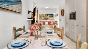 Un comedor con una mesa lista para cuatro personas, un florero con flores y un cuadro en la pared.