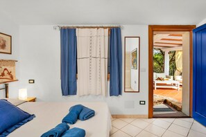 Quarto com cama, toalhas, cortinas, espelho e vista para um pátio.